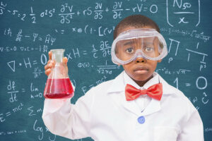 Boy wearing protective glasses holding a beaker against black board